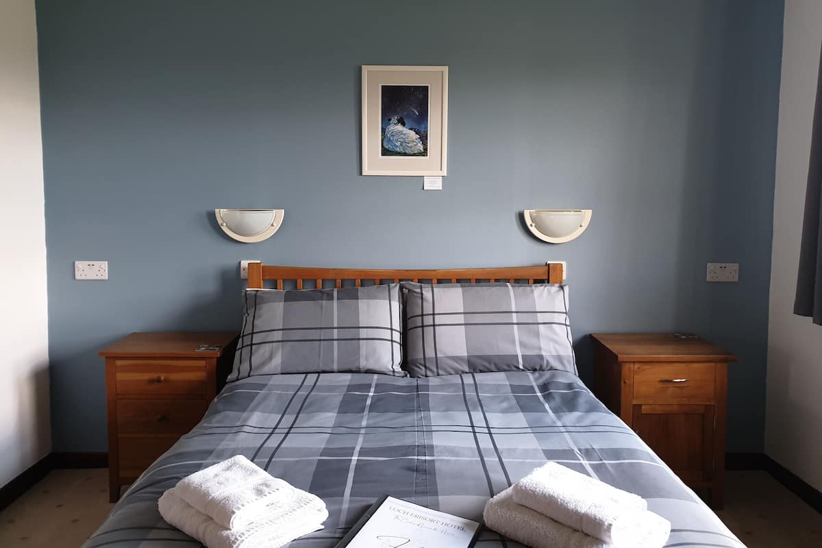 A neatly made bed with a checkered bedspread, two bedside tables, and a framed picture on the wall.