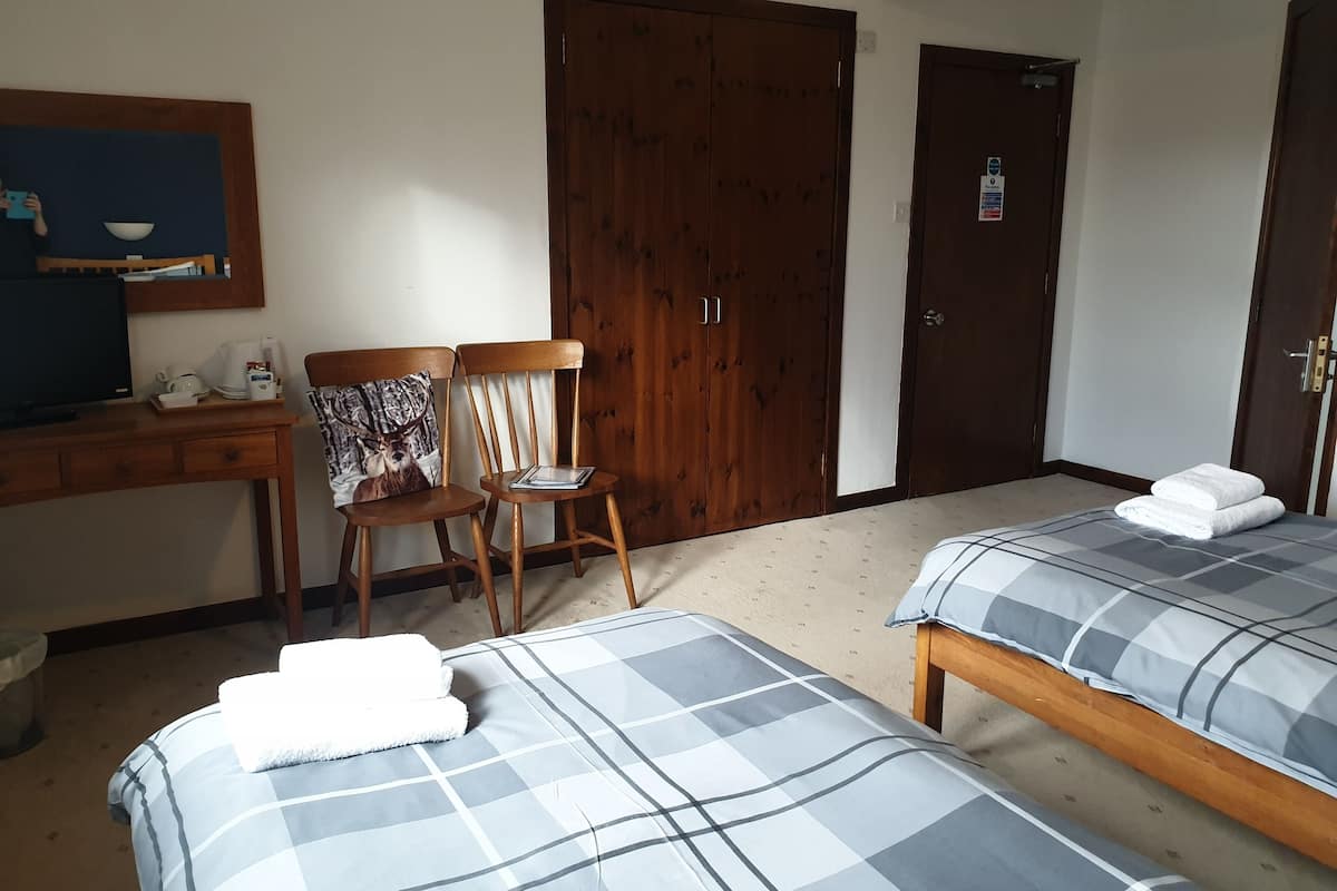 A hotel room with two beds, a desk with a computer, a chair, and a wardrobe.