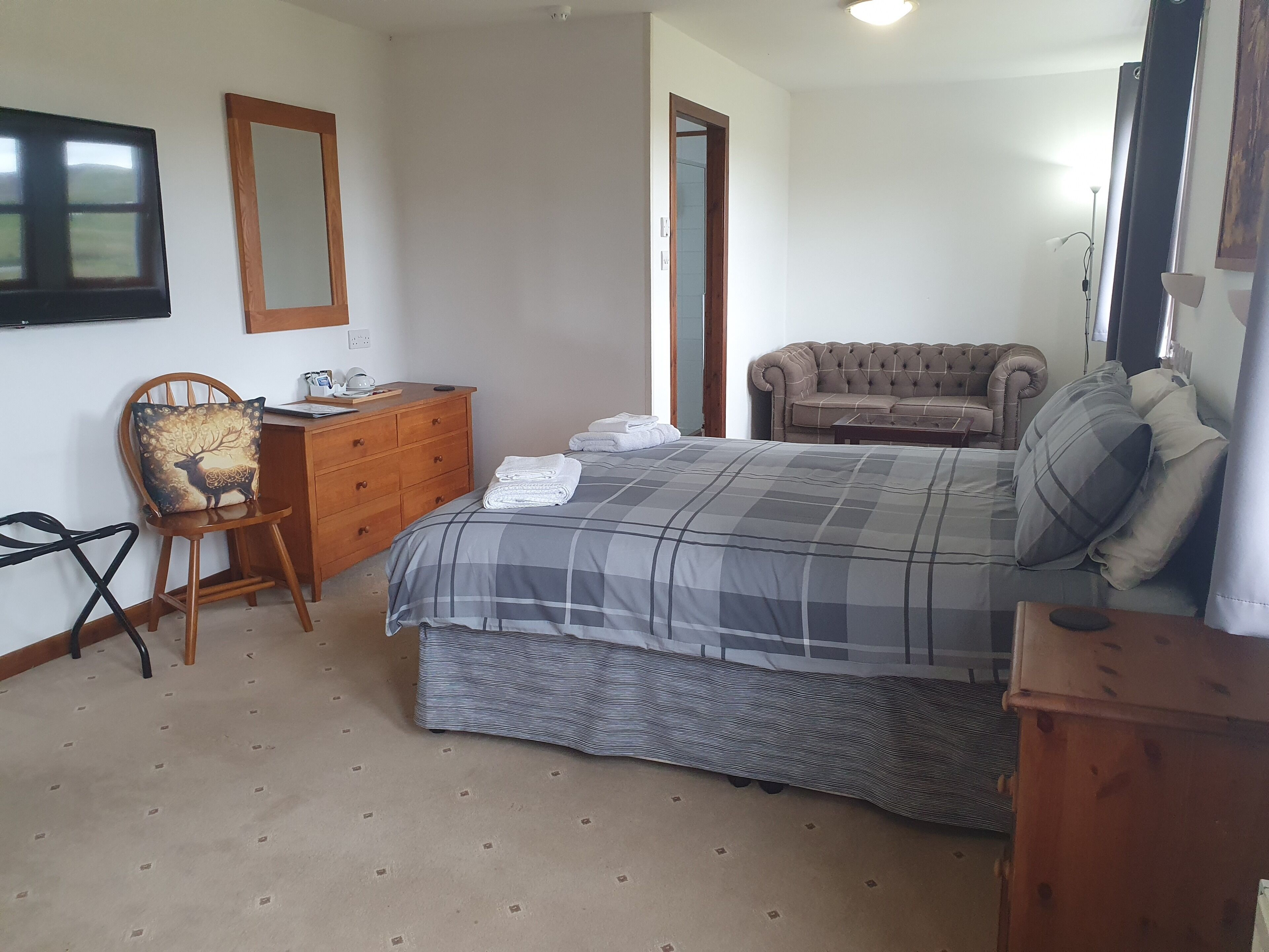 A bedroom with a bed, a dresser, a chair, a sofa, and a television.
