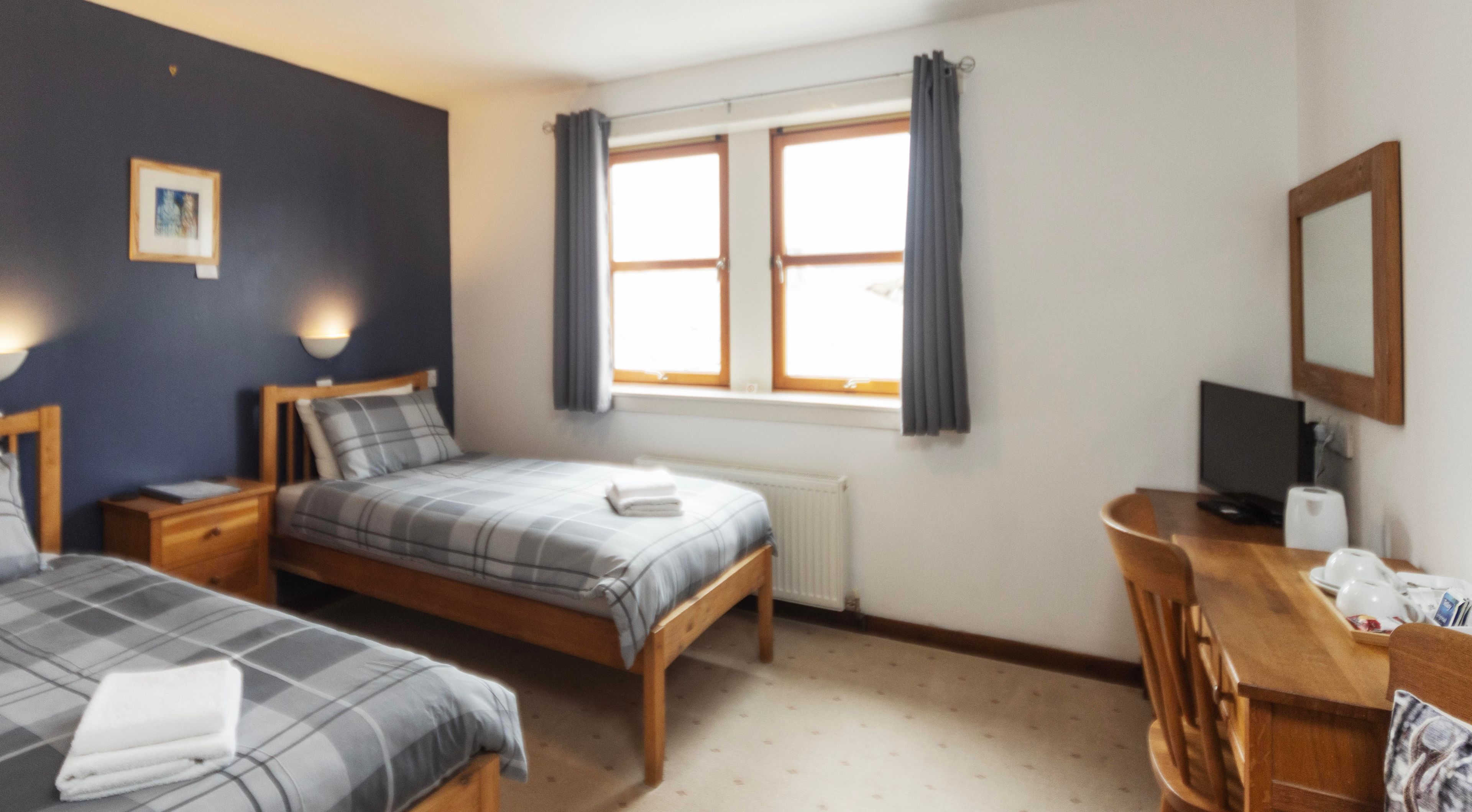 Un dormitorio con dos camas, un escritorio, una silla, un radiador y una ventana con cortinas.