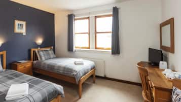 Un dormitorio con dos camas, un escritorio, una silla, un radiador y una ventana con cortinas.