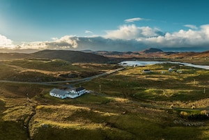 An aerial view of a rural landscape with a white house, a small body of water, and rolling hills.