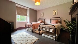 Quarto com duas camas de metal, uma janela com vista, um radiador e uma planta.