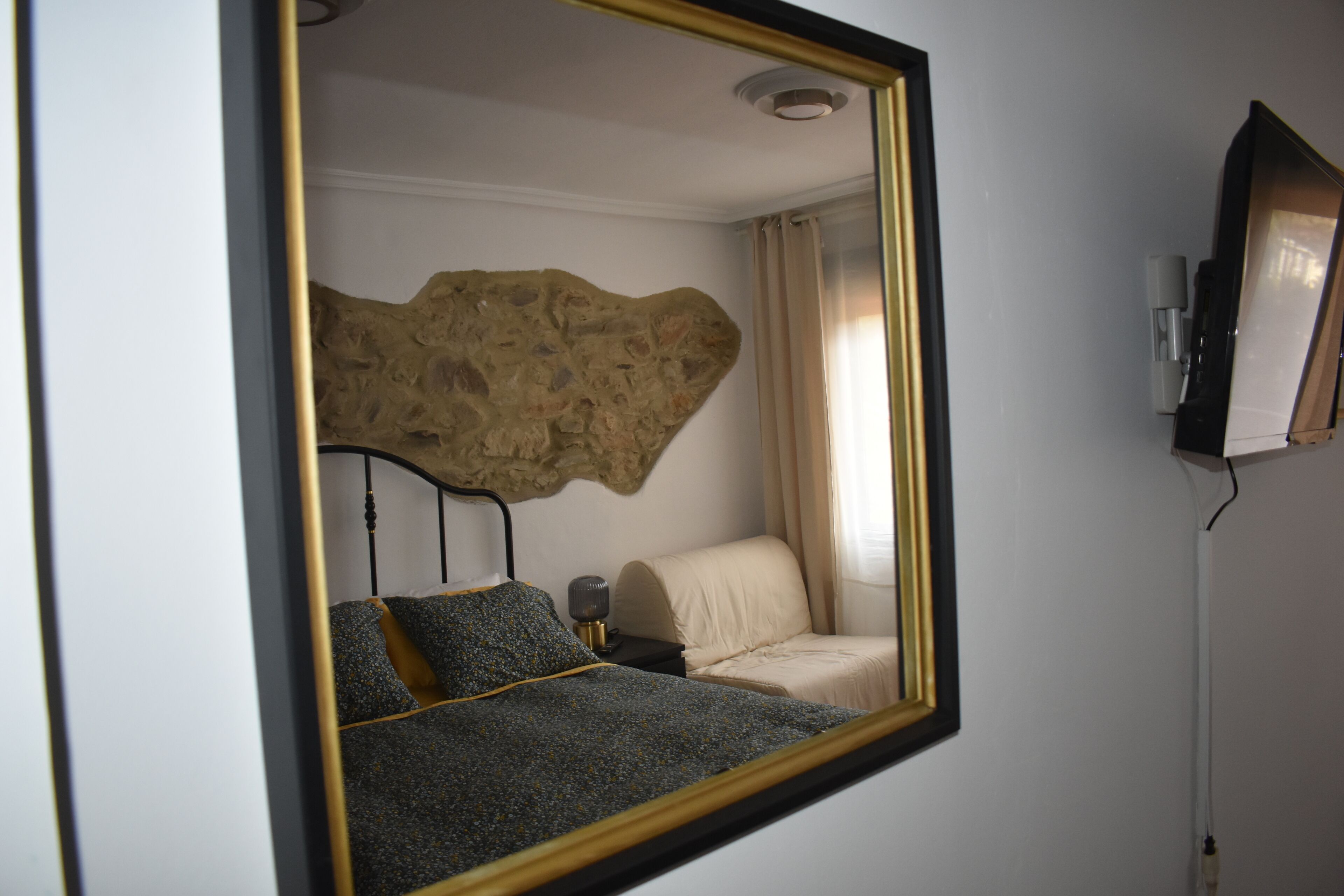 A bedroom with a bed, a nightstand, a lamp, a wall-mounted TV, and a stone accent wall.