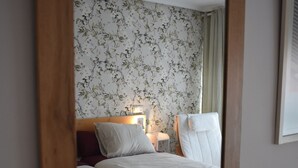 Un dormitorio con dos camas, papel tapiz floral, una lámpara de noche y un cabecero de madera.
