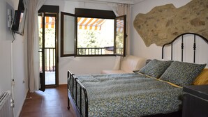 Un dormitorio con cama, ventana con cortinas, pared de piedra y vistas al exterior.