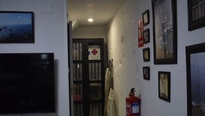 Un pasillo con un televisor montado en la pared izquierda, un extintor en la derecha y cuadros enmarcados a lo largo de las paredes.