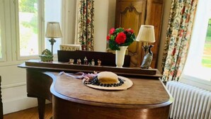 A wooden piano with a bench, a lamp, a vase with flowers, and a painting on the wall.