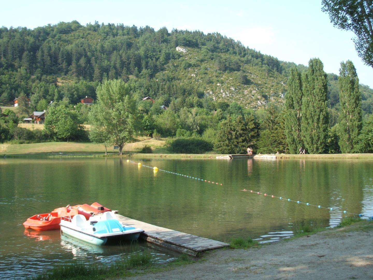 A lake with boats docked, surrounded by forested hills and houses.