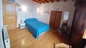 A bedroom with a wooden ceiling, a bed with a blue bedspread, a wardrobe, a chair, and a radiator.