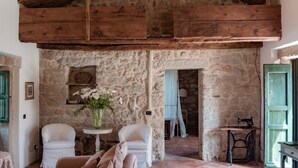 A rustic interior with stone walls, wooden beams, a tiled floor, a sofa, two chairs, a table with a vase, and a sewing machine. - 3 Bedroom Private vacation home in Arzachena (Arzachena)