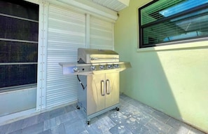 A portable gas grill with four burners, a side burner, and a lid, placed on a wheeled cart. - Coastal Charm with Heated Pool (Cape Coral)