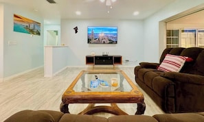 A living room with a glass coffee table, a brown sofa, a television, and a painting on the wall. - Coastal Charm with Heated Pool (Cape Coral)