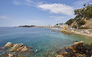 A coastal view with clear waters, rocky shoreline, and buildings along the beach.