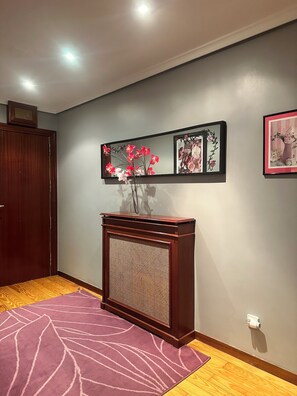 A hallway with a wooden door, a console table with a vase of flowers, and two framed pictures on the wall.