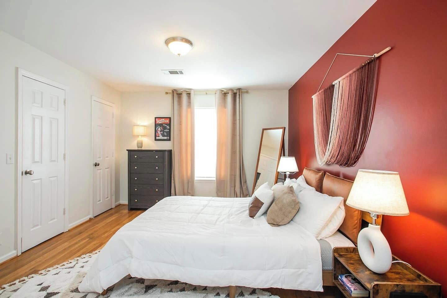 A bedroom with a bed, a dresser, a nightstand, a mirror, and a window with curtains.