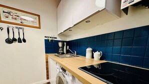 Cocina compacta con lavadora, cafetera y hervidor sobre la encimera.