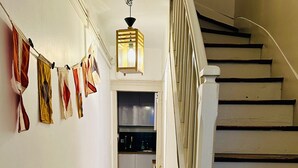 Una escalera con escalones de madera y barandillas blancas que lleva a un área de cocina con armarios y una lámpara colgante.