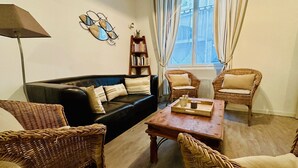 Una sala de estar con un sofá negro, sillas de mimbre, una mesa de centro de madera y una estantería.