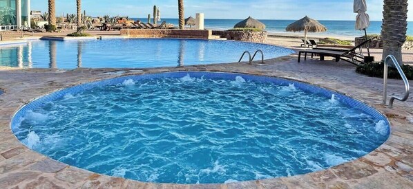 Piscina com hidromassagem, espreguiçadeiras e vista para a praia.