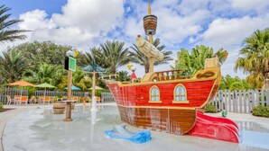 A pirate ship-themed water play area with a slide, surrounded by palm trees and outdoor seating.