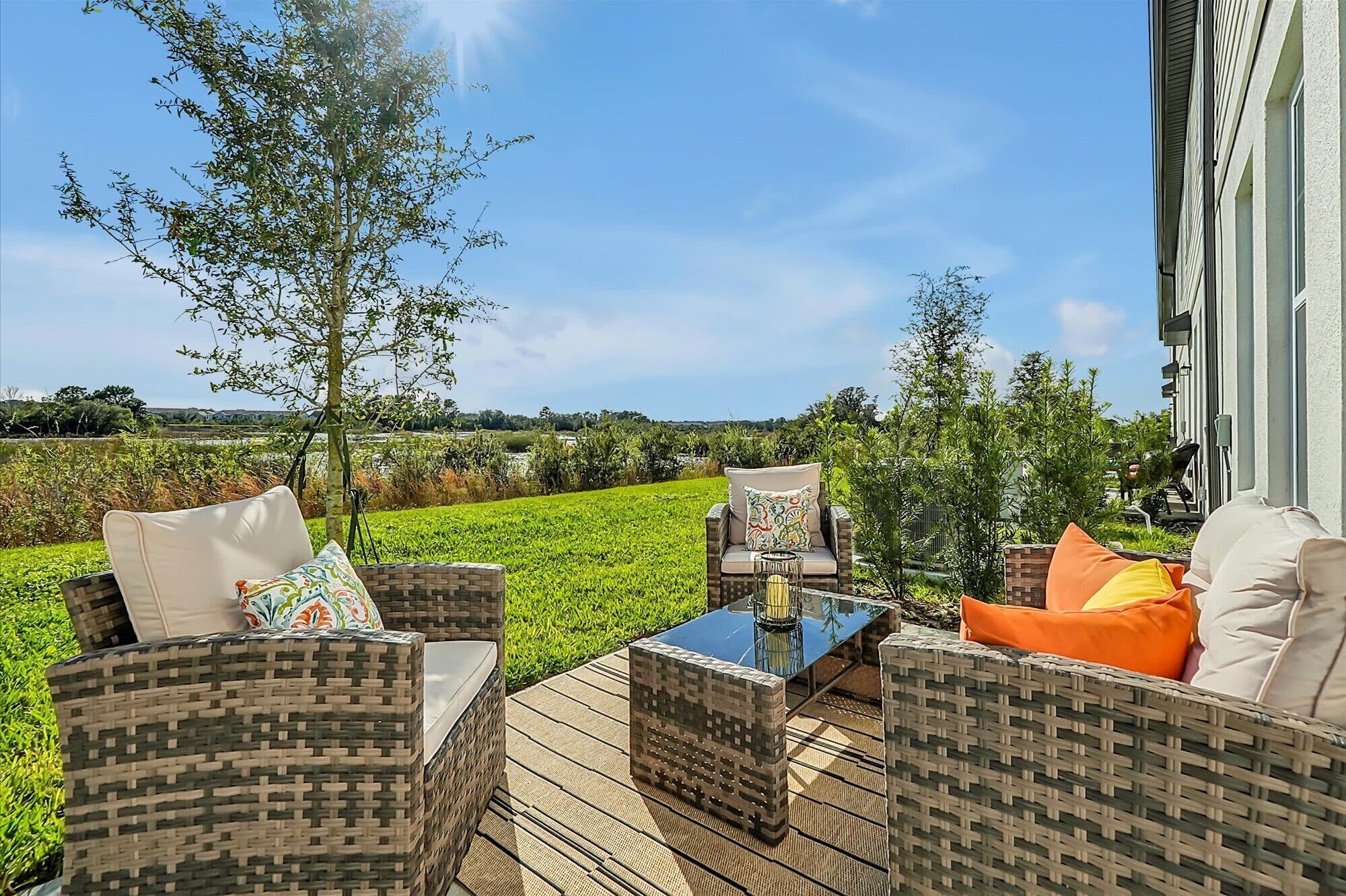 An outdoor patio with wicker furniture, a glass table, and a view of a green field and distant landscape.