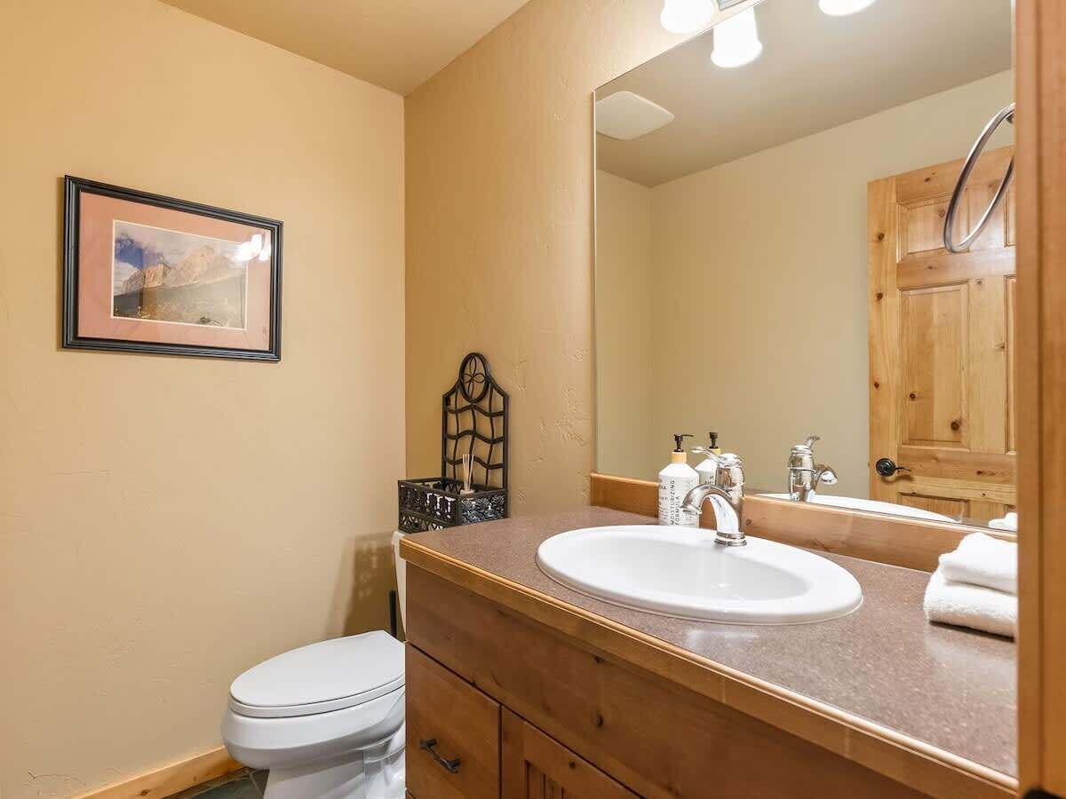 A bathroom with a white toilet, a sink with a mirror above it, and a framed picture on the wall.