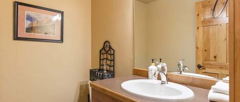 A bathroom with a white toilet, a sink with a mirror above it, and a framed picture on the wall.