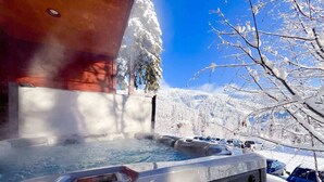 A hot tub with a wooden structure, surrounded by snow-covered trees and a clear blue sky. - Amazing Mountain View | Ski Access | Hot Tub & Sauna (Whitefish)