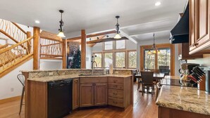 A kitchen with a wooden island, built-in appliances, and a dining area with a wooden staircase. - Amazing Mountain View | Ski Access | Hot Tub & Sauna (Whitefish)