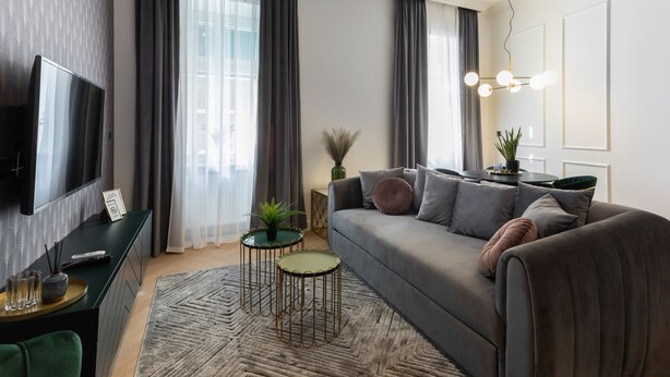 A modern living room with a grey sofa, a TV, and a dining area with a table and chairs. - Candy Cavalier Zagreb Center Lux (Zagreb)