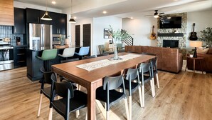 A modern kitchen with stainless steel appliances, a dining area with a wooden table and chairs, and a living room with a fireplace and a television. - Legends Pointe | Hot tub, Lake view, Theatre, Pool table, Dog-friendly (Hollister)
