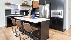 A modern kitchen with black cabinets, stainless steel appliances, and a central island with bar stools. - Heated private pools, Lake views, Wheelchair friendly | The Cottages (Hollister)