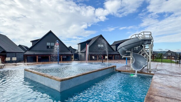 A swimming pool with a water slide, surrounded by buildings with dark roofs and a clear sky. - Heated private pools, Lake views, Wheelchair friendly | The Cottages (Hollister)