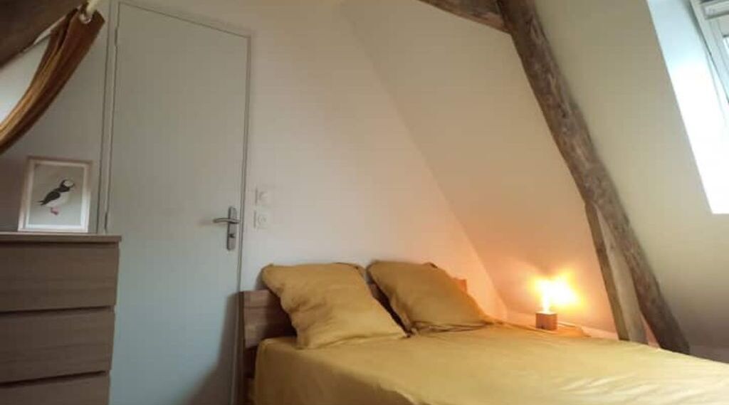 A bedroom with a bed, a bedside table, a nightstand, a framed picture, and a window with curtains.