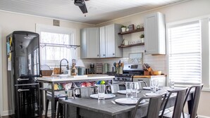 A kitchen with a central island, white cabinets, a black refrigerator, and a dining area with chairs and a table set for four. - Downtown NB Cottage, Backyard, Fire Pit, walkable (New Buffalo)