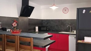 A modern kitchen with a central island, red cabinets, a black refrigerator, and a microwave.