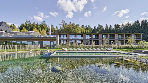 A modern building with a swimming pool, clear water, and a wooden deck. - Hotel Munde (Hofstetten)