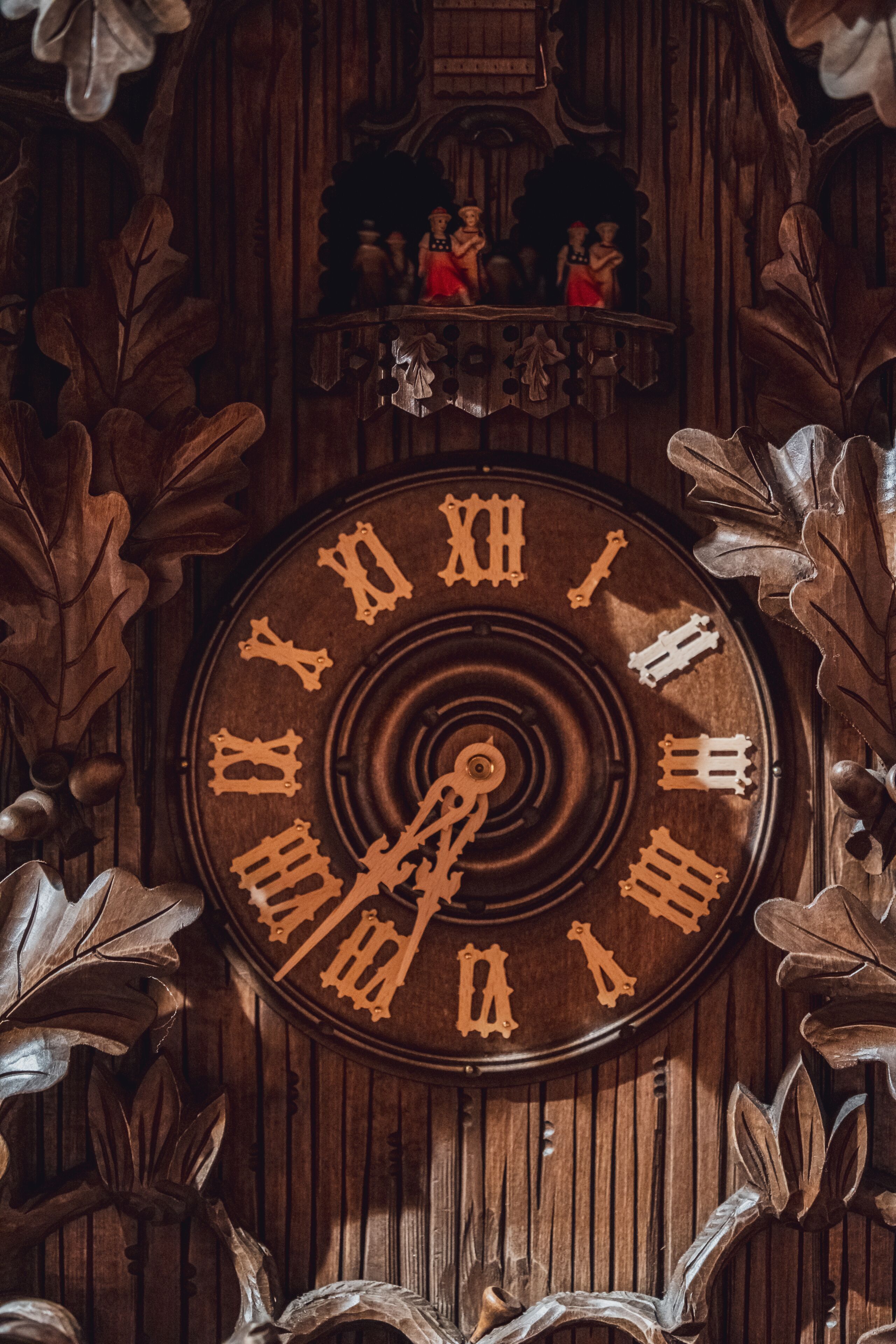 Un reloj de madera con números romanos y un péndulo, rodeado de motivos de hojas talladas.