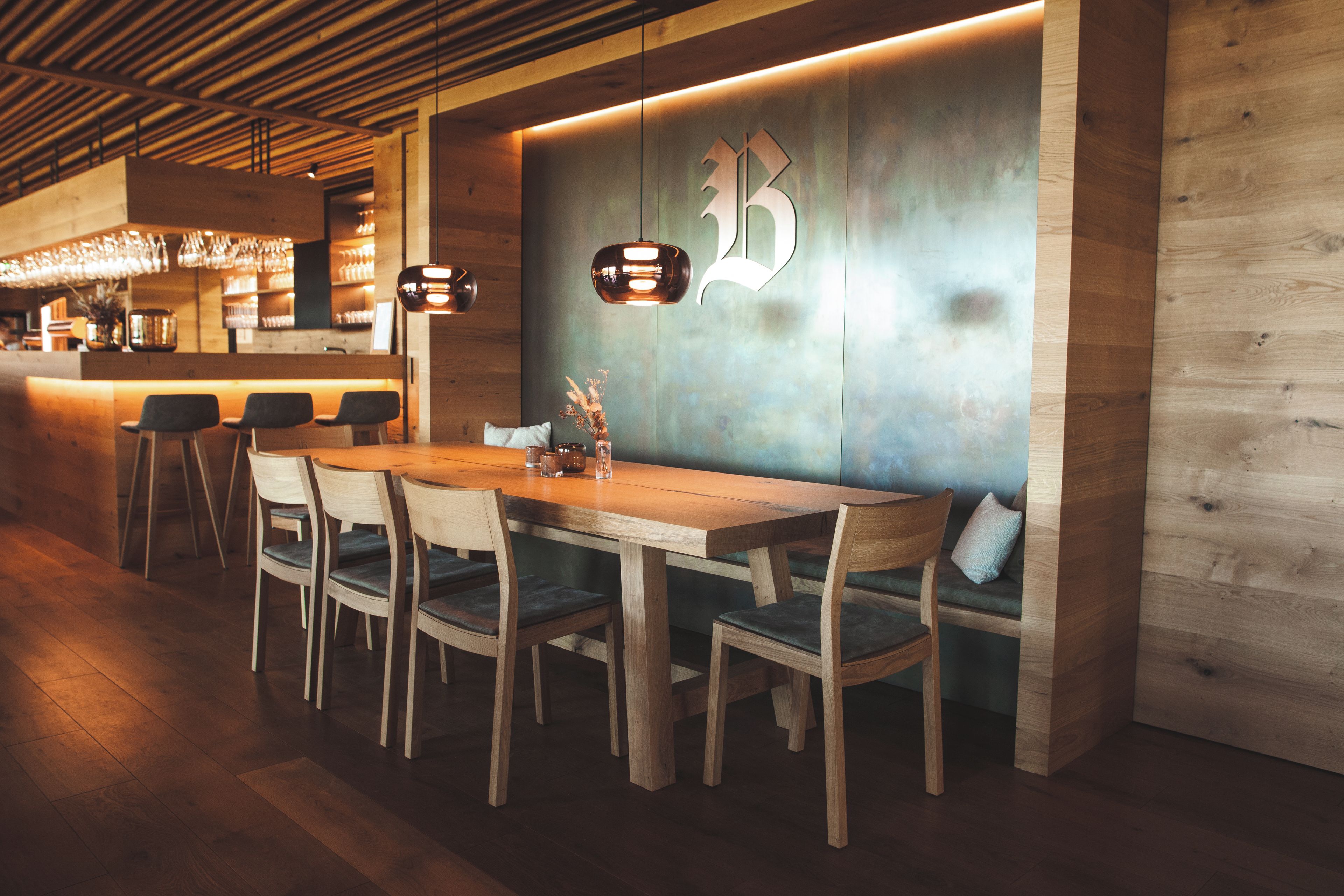 Un comedor moderno con una mesa y sillas de madera, una barra con vasos, y una pared con un logotipo.