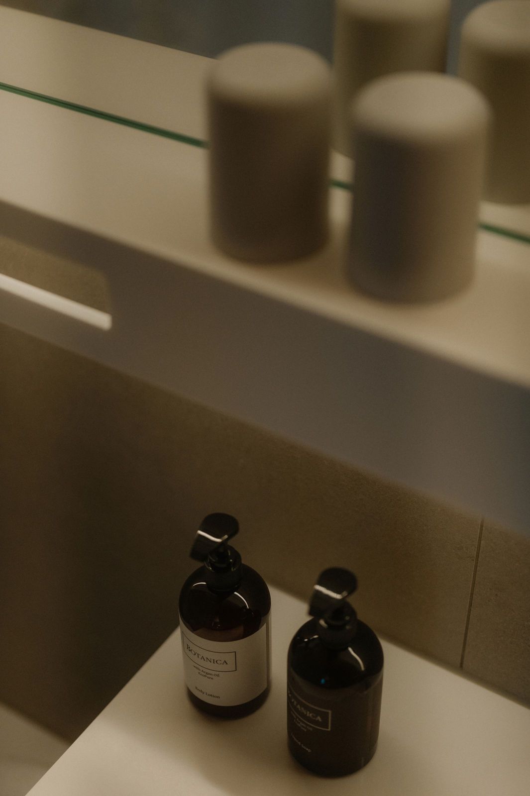 Una encimera de baño con dos botellas de loción y un espejo encima.