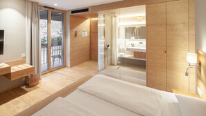 A modern hotel room with a wooden floor, a large bed, a glass shower enclosure, a balcony with a chair, and a wooden wardrobe. - Hotel Munde (Hofstetten)