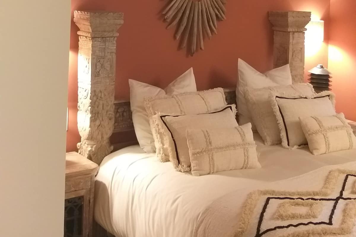 A bedroom with a large bed, a decorative wall piece, and two nightstands with lamps.