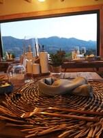 Una mesa de comedor con un mantel tejido, cristalería y vistas a montañas a través de una ventana.