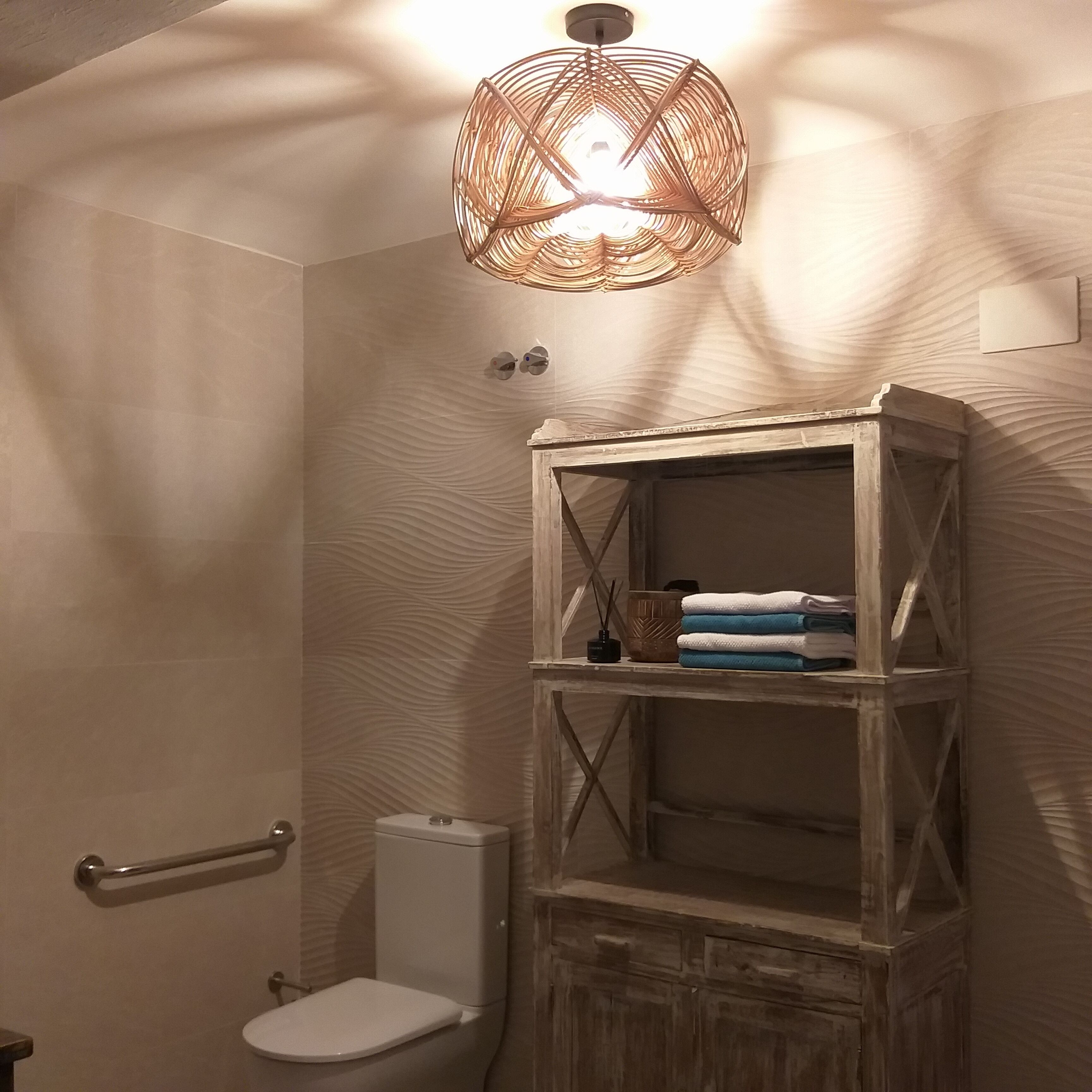 Ein Badezimmer mit einer weißen Toilette, einem Holzregal mit Handtüchern und einer außergewöhnlichen gewebten Lampe.