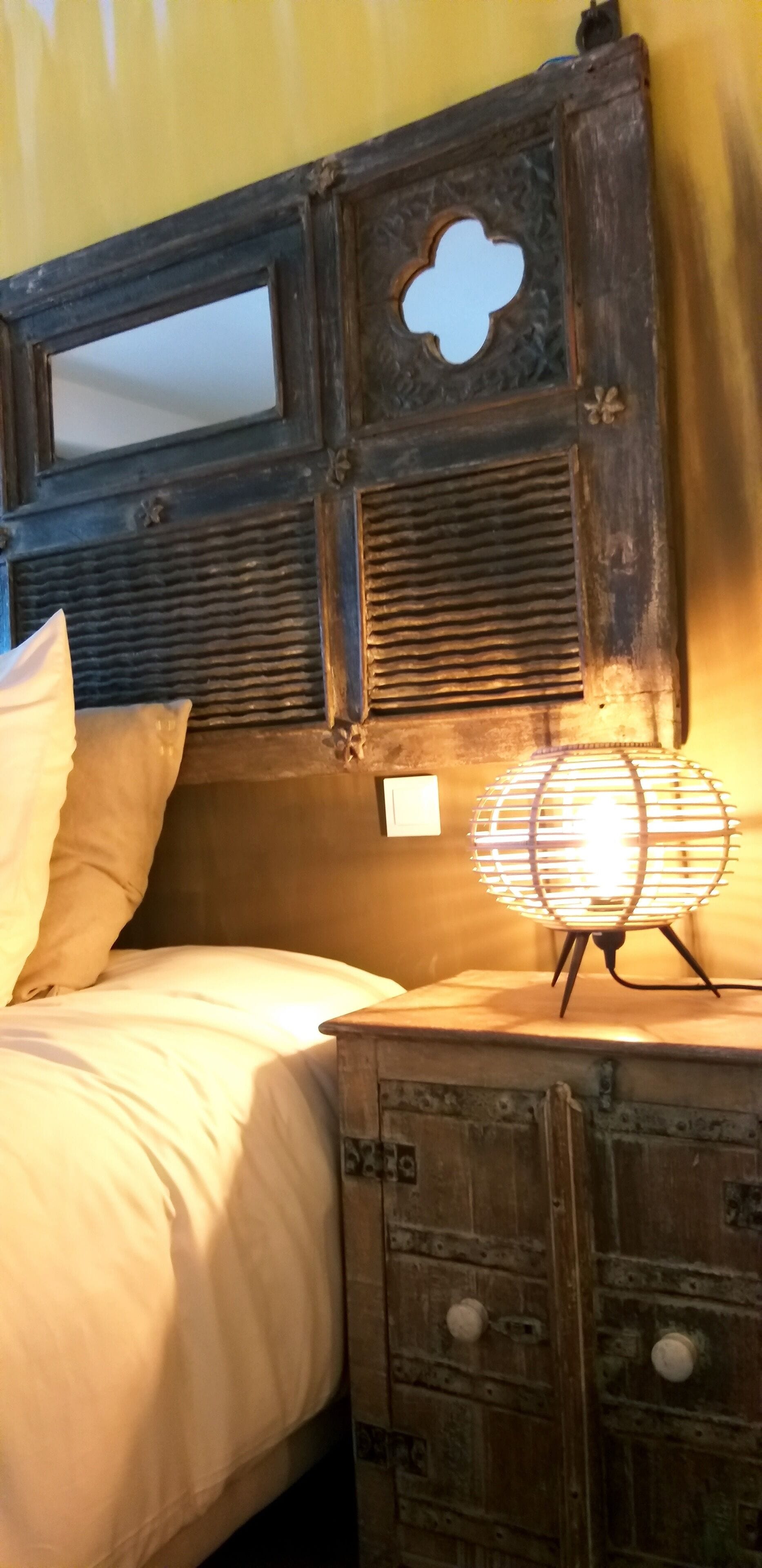 A bed with white linens, a wooden headboard with a decorative cut-out, and a bedside lamp.