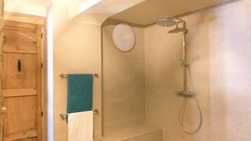 Un baño con puerta de madera, ducha con cabezal de ducha manual y un perchero con dos toallas.
