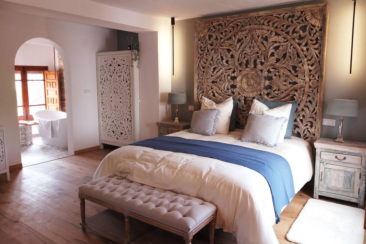 A bedroom with a large bed, a bench, a wardrobe, and a decorative headboard.