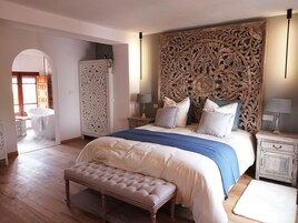 Un dormitorio con una cama grande, una banca, un armario y un cabecero decorativo.