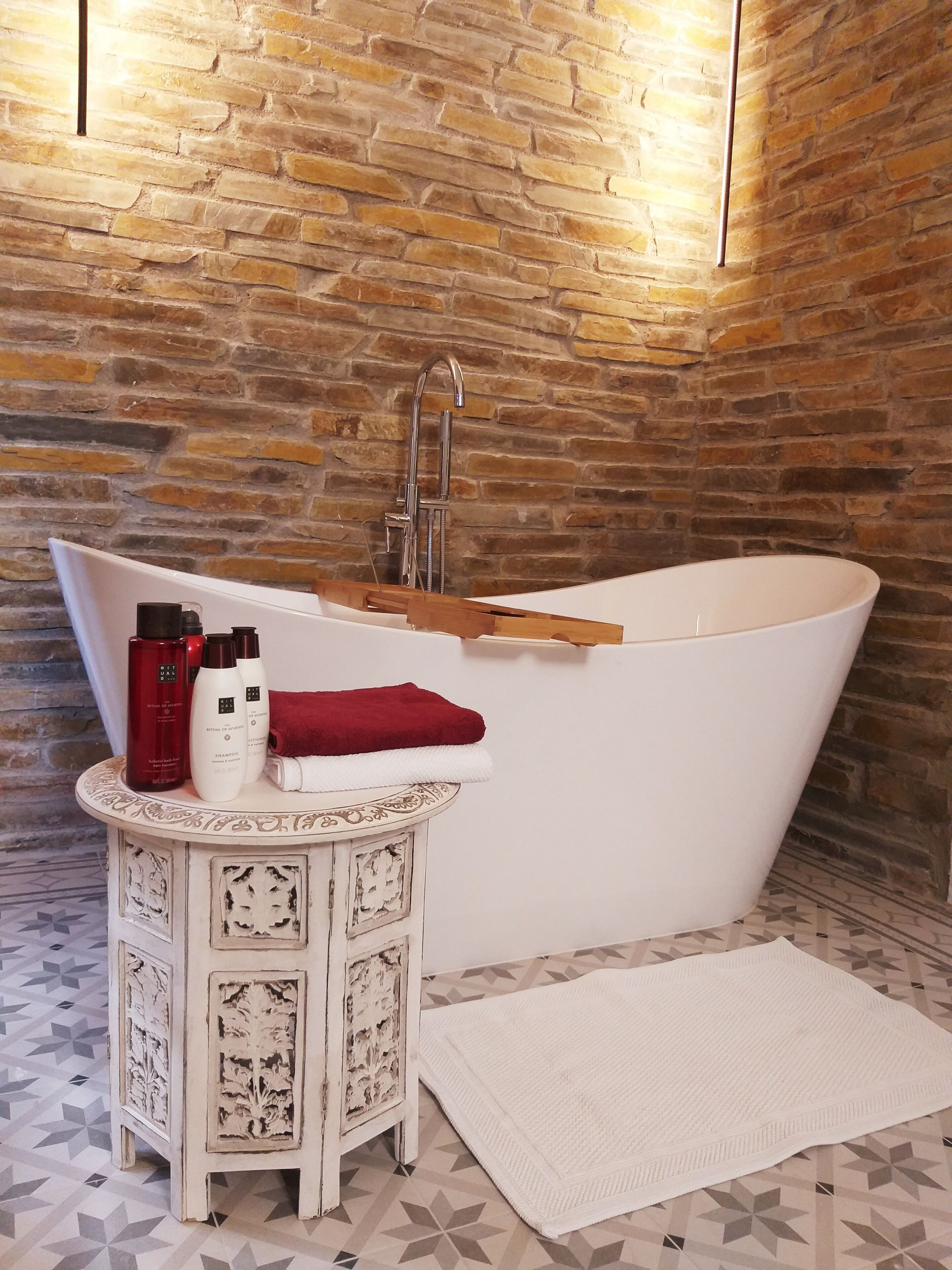 Un baño con una bañera independiente, un tocador pequeño con un espejo decorativo y un suelo estampado.